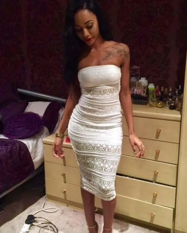 Femme noire en robe blanche moulante, chambre violette, regard baissé