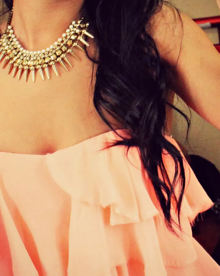 Femme brune en collier à pointes, top rose fluide, pose spontanée