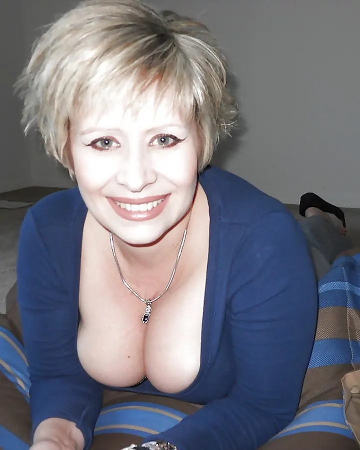 Femme blonde courte, décolleté plongeant, allongée sur coussins rayés