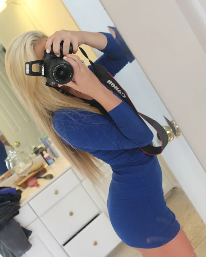 Jeune femme blonde en robe bleue moulante, appareil photo à la main, miroir selfie