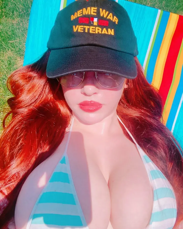 Femme aux cheveux roux portant un maillot de bain rayé et une casquette, allongée sur une couverture colorée en extérieur.