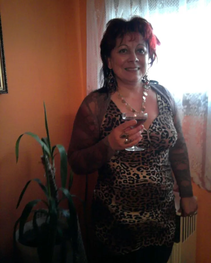 Femme aux cheveux roux en tenue léopard tenant un verre de vin près d'une fenêtre