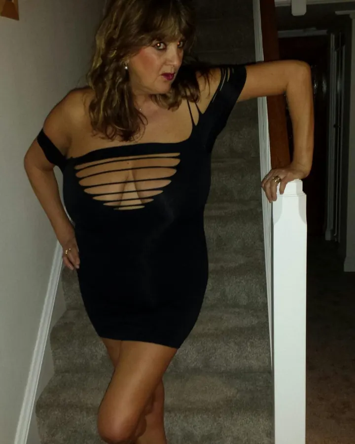 Femme aux cheveux bruns en robe noire moulante sur un escalier intérieur