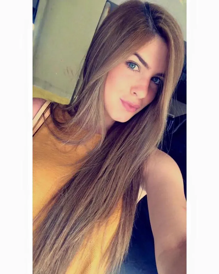 Femme blonde, souriante, portant un haut noir transparent, prenant une photo de profil devant un miroir.