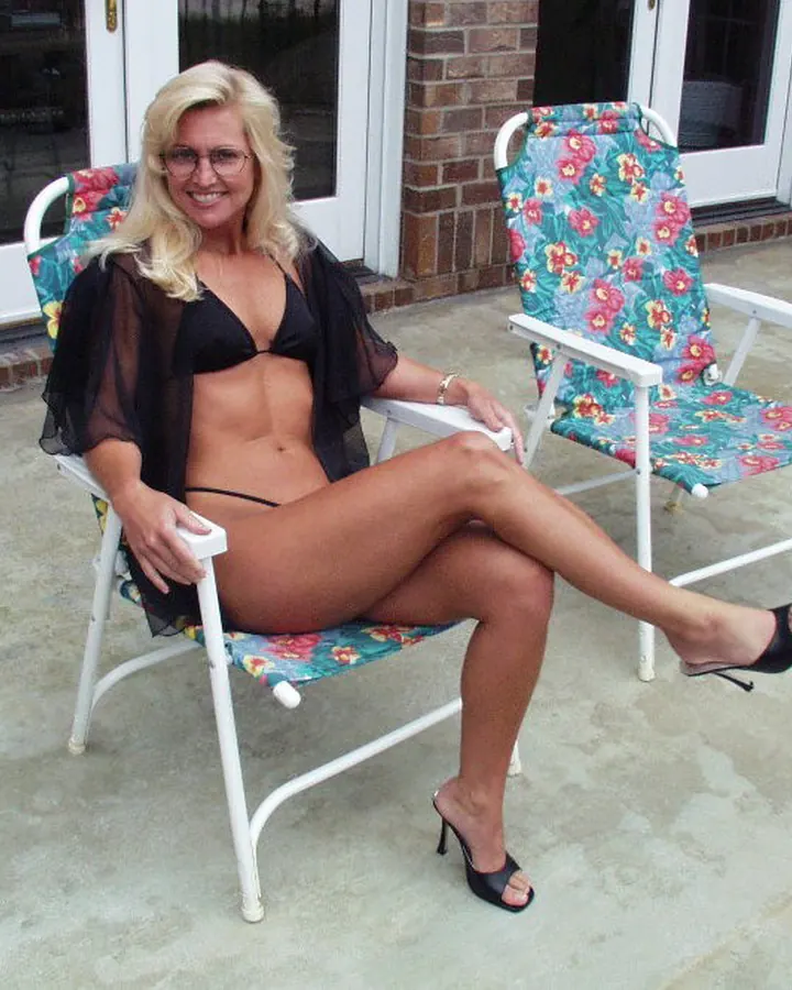 Femme blonde, souriante, portant un haut noir transparent, prenant une photo de profil devant un miroir.