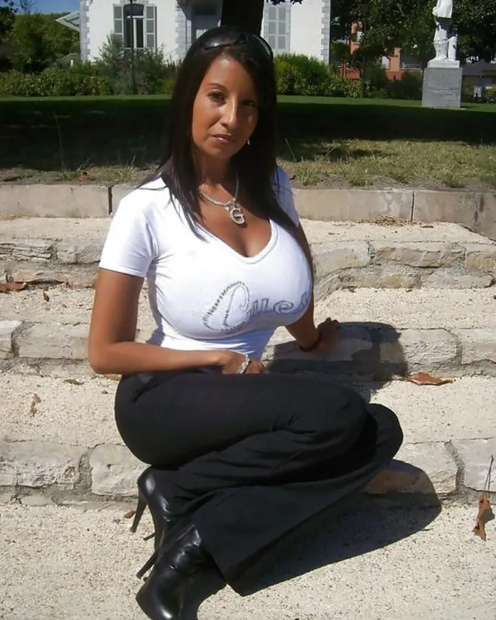 Femme aux cheveux bruns-noirs portant un haut noir, souriant à la caméra.