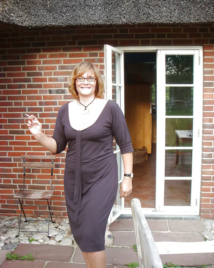 Femme aux lunettes et robe marron devant une maison en briques