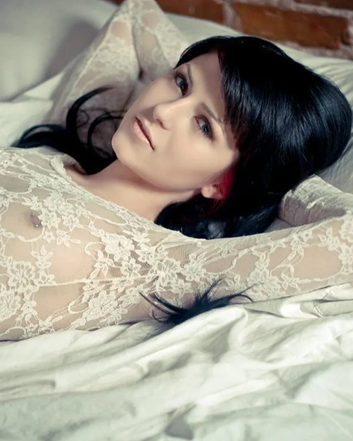 Femme brune en body en dentelle allongée sur un lit