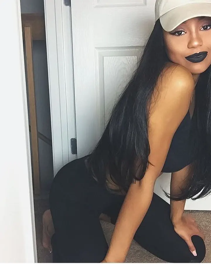 Femme à casquette et maquillage sombre, accroupie près d’une porte blanche