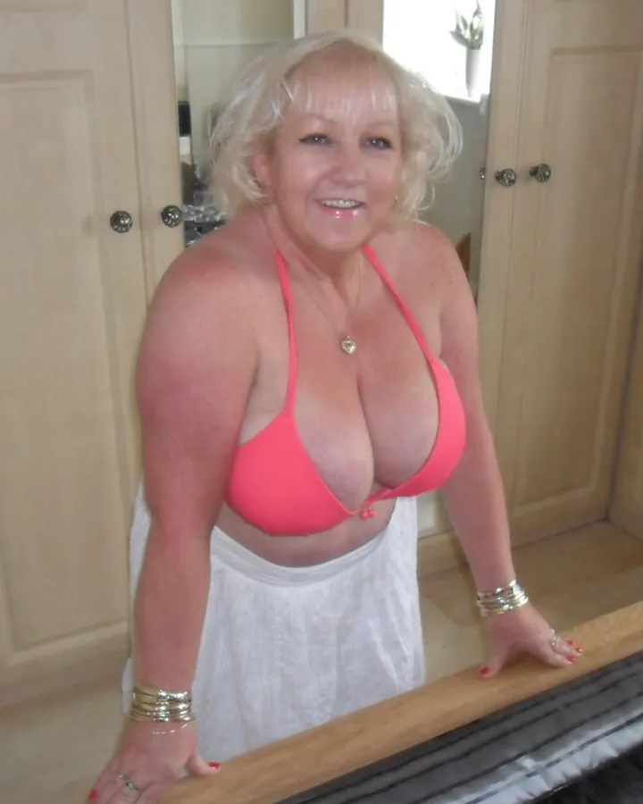 Femme blonde en bikini rose prenant un selfie sur une plage.