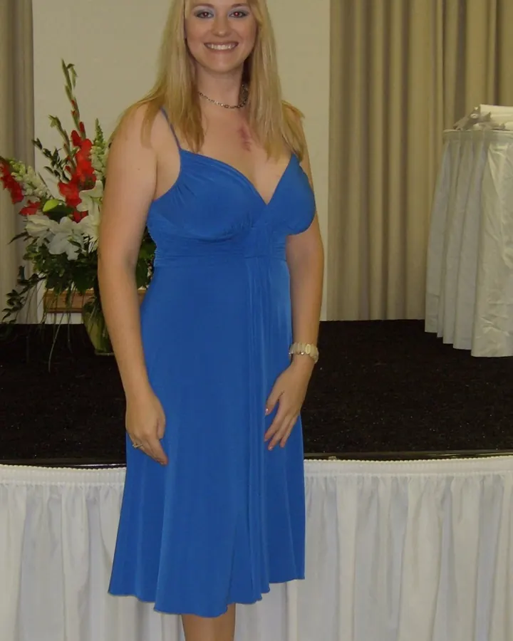 Jeune femme blonde en robe bleue, debout devant une estrade fleurie