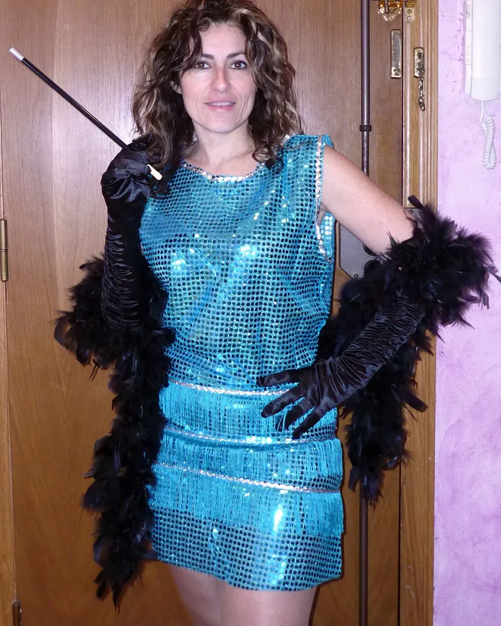 Femme brune en robe courte turquoise à sequins, gants noirs et plumeau