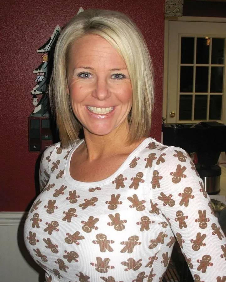 Femme blonde aux cheveux courts, pull blanc à motifs pain d’épice, sourire franc
