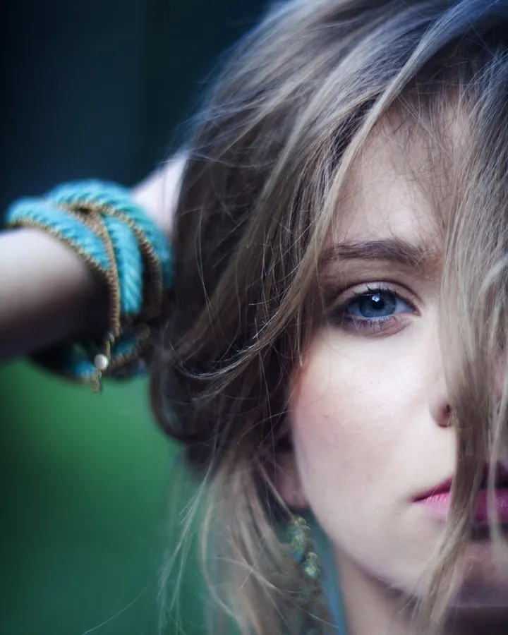 Jeune femme aux cheveux châtains, en robe rose, posant dans un champ de bottes de foin sous un ciel bleu.