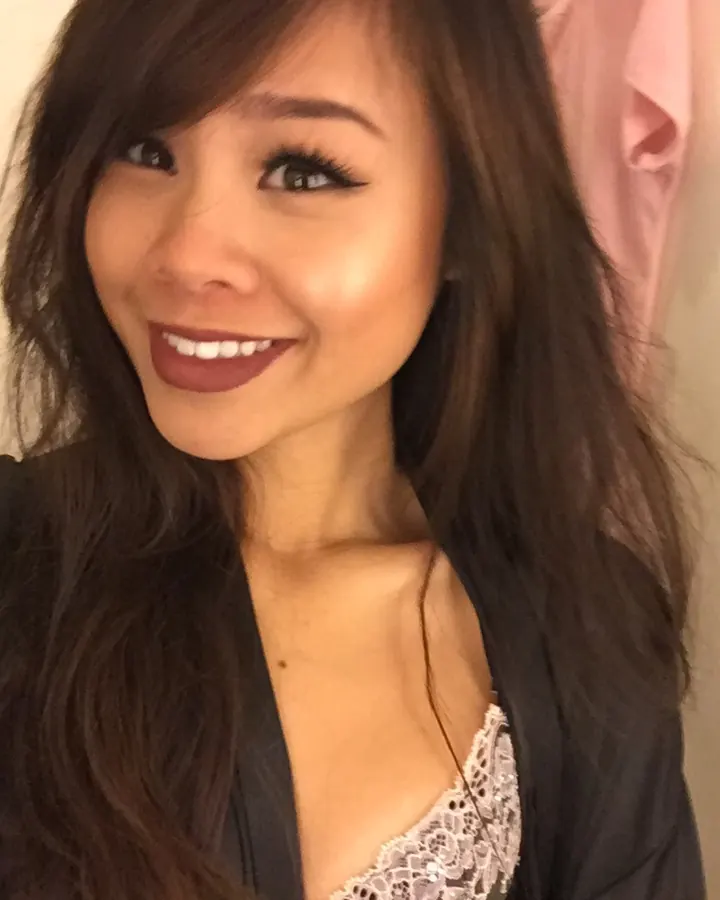 Femme asiatique souriante, en veste noire, avec un décolleté en dentelle blanche.