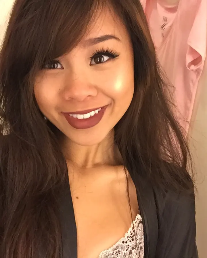 Femme asiatique souriante, en veste noire, avec un décolleté en dentelle blanche.