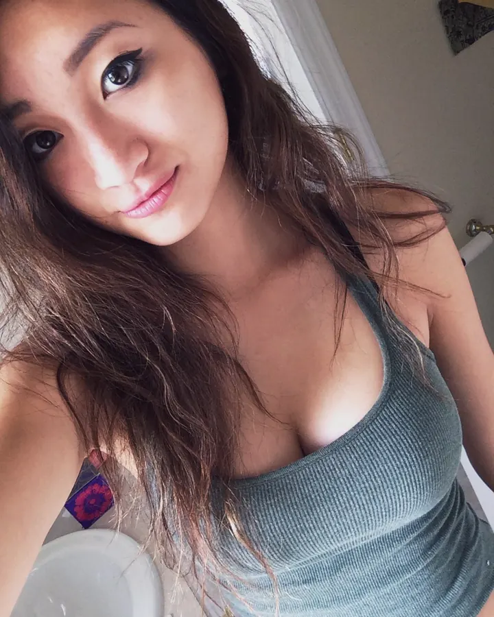 Femme aux cheveux longs prenant un selfie dans un miroir, portant un haut noir et un short noir à bordure blanche, dans une chambre bleue.