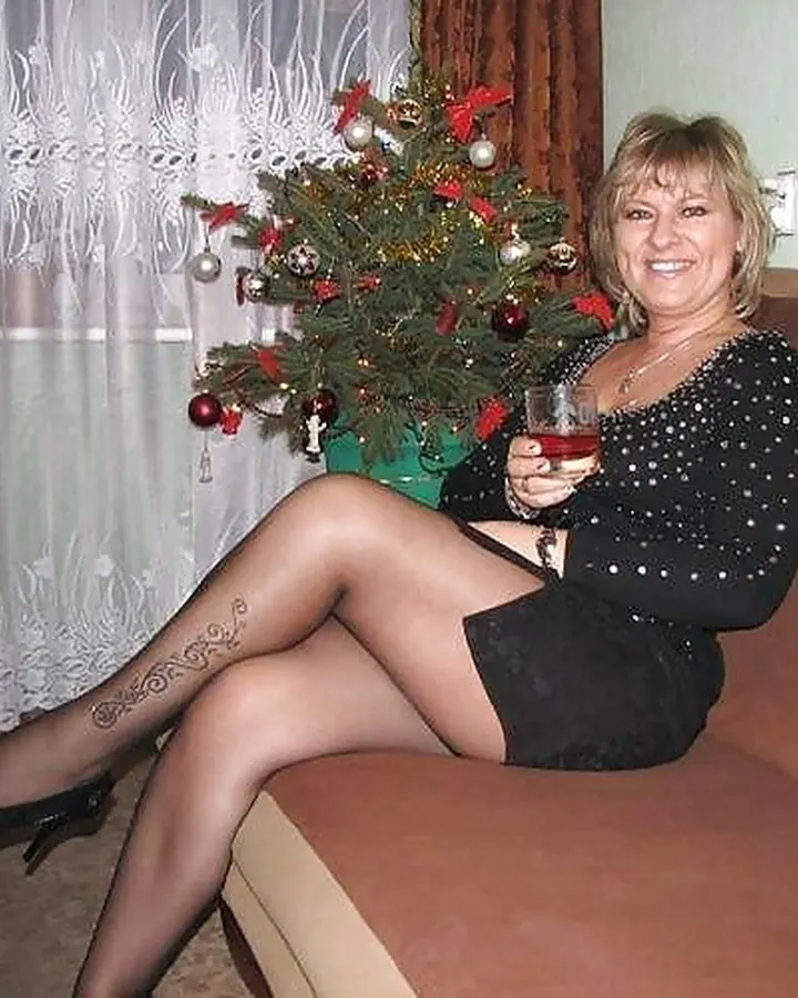 Femme aux cheveux blonds, portant un haut noir, assise sur un canapé, regardant vers le bas.
