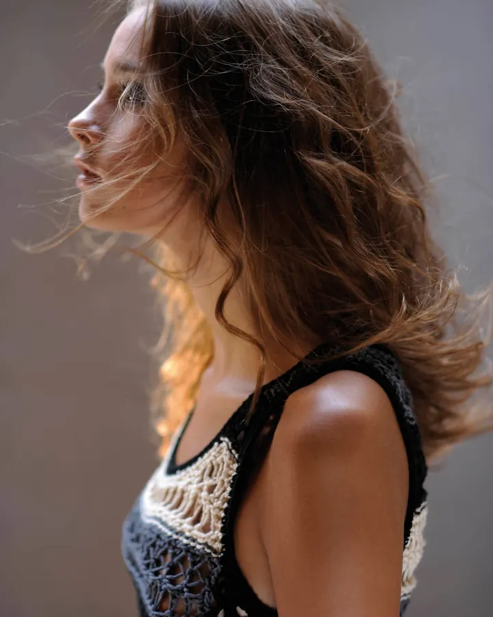 Femme aux cheveux bruns, portant un haut noir, assise sur un canapé, regardant vers le bas.