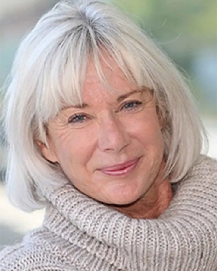 Femme aux cheveux blancs, souriante, portant un pull tricoté beige en extérieur