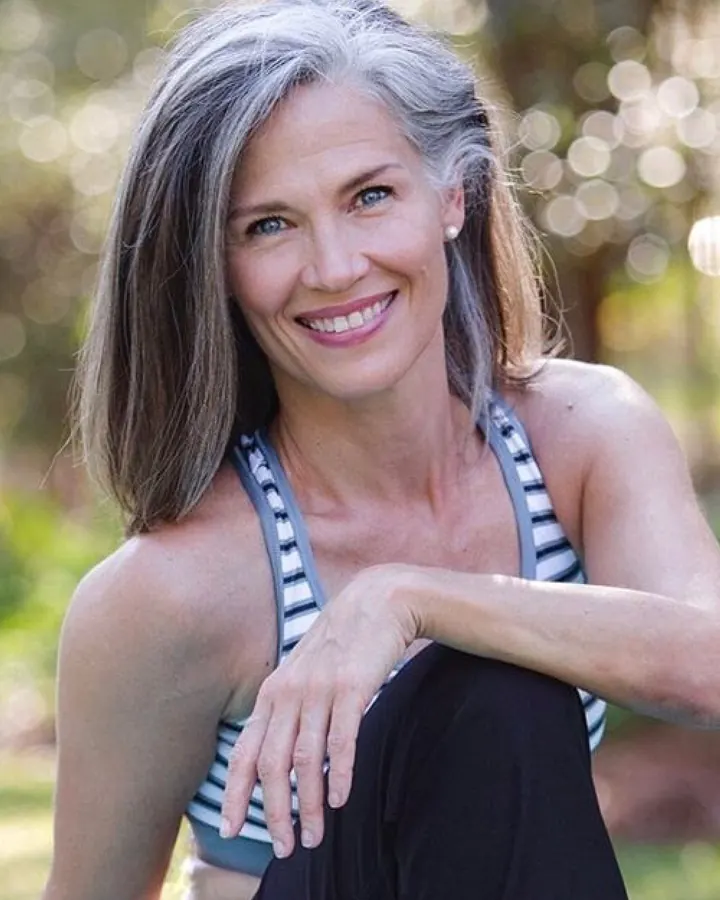 Femme aux cheveux gris, souriante, portant un haut noir avec un collier en perles