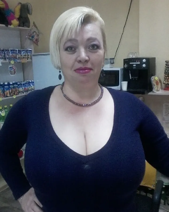 Femme blonde aux yeux marrons, regardant l'appareil photo, portant un haut noir avec un collier en perles