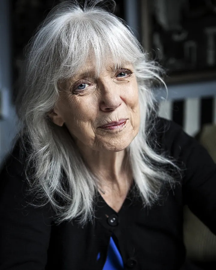 Femme aux cheveux platine, souriante, portant un haut noir avec un collier en perles