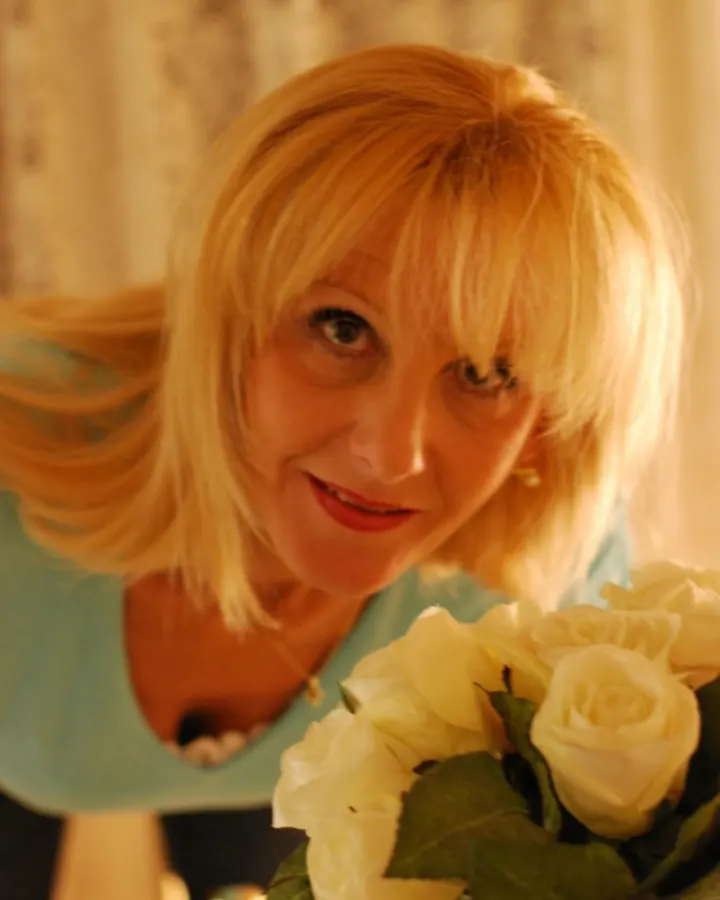 Femme blonde aux yeux bleus, souriante, tenant un bouquet de roses blanches en intérieur