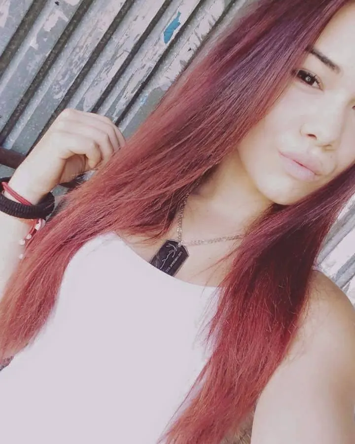 Femme aux cheveux roux portant un haut blanc, devant un mur en bois vieilli