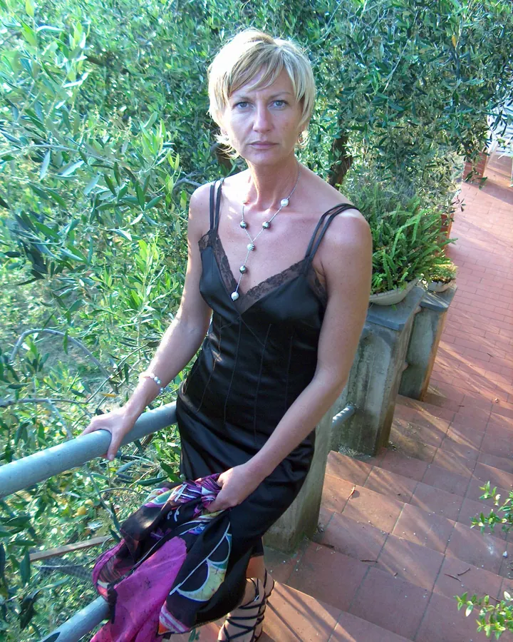 Femme blonde, en robe noire, assise sur un balcon entouré de verdure