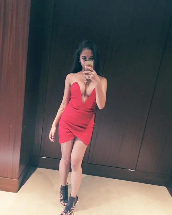 Femme en robe rouge moulante, prenant un selfie devant un miroir, cheveux noirs longs, chaussures à talons noirs