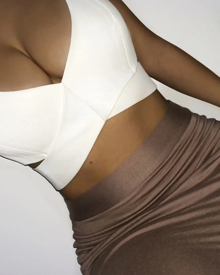 Plan rapproché d'une femme aux cheveux noirs, portant un haut blanc et une jupe marron, montrant sa taille et ses hanches.