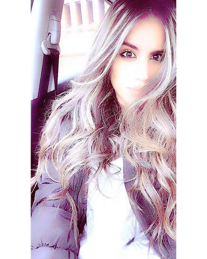 Femme aux cheveux gris, portant un haut noir et un short en jean, prenant un selfie dans un dressing.