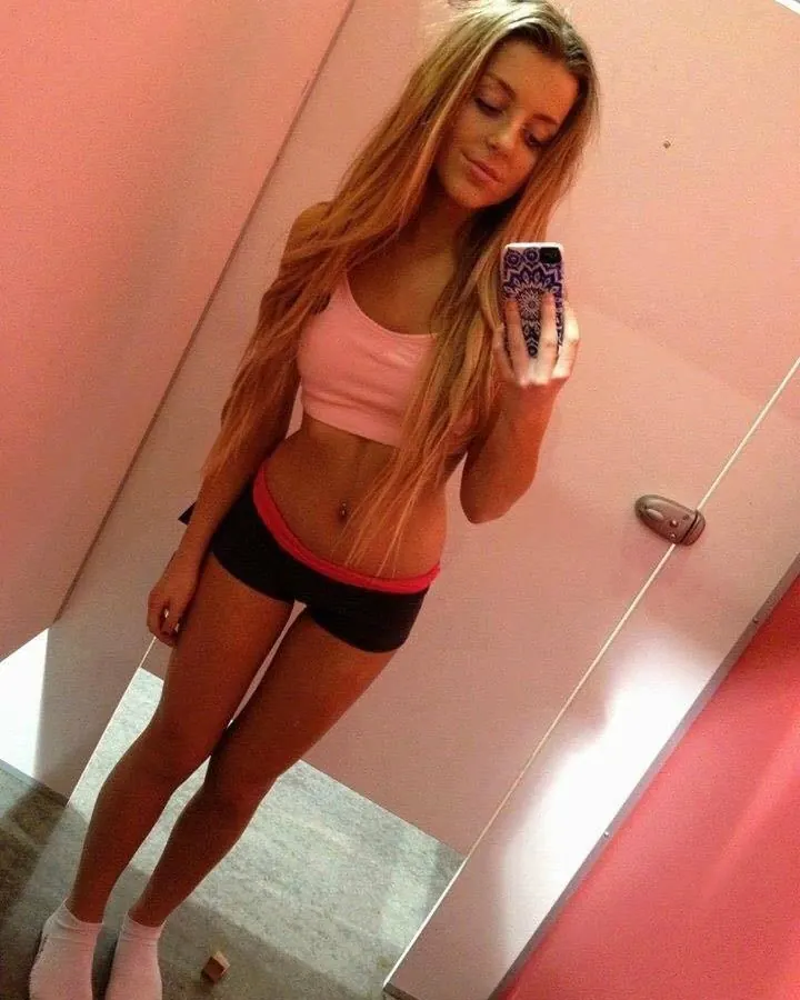 Femme aux cheveux bruns, portant un haut noir, tenant un club de golf, debout devant un buisson de fleurs roses.