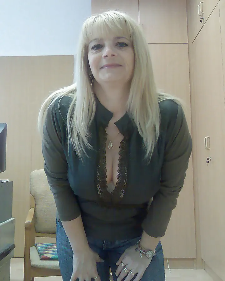 Femme aux cheveux roux bouclés, portant une robe courte camouflage jaune et gris, collants verts et chaussures noires, dans un salon.