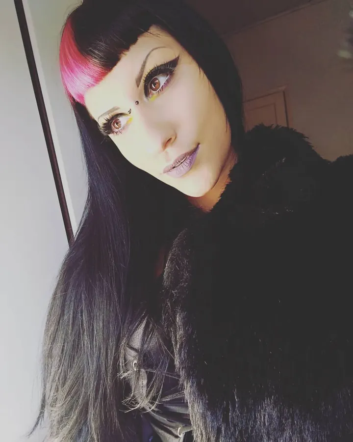 Femme brune en tenue noire, regard direct, maquillage prononcé