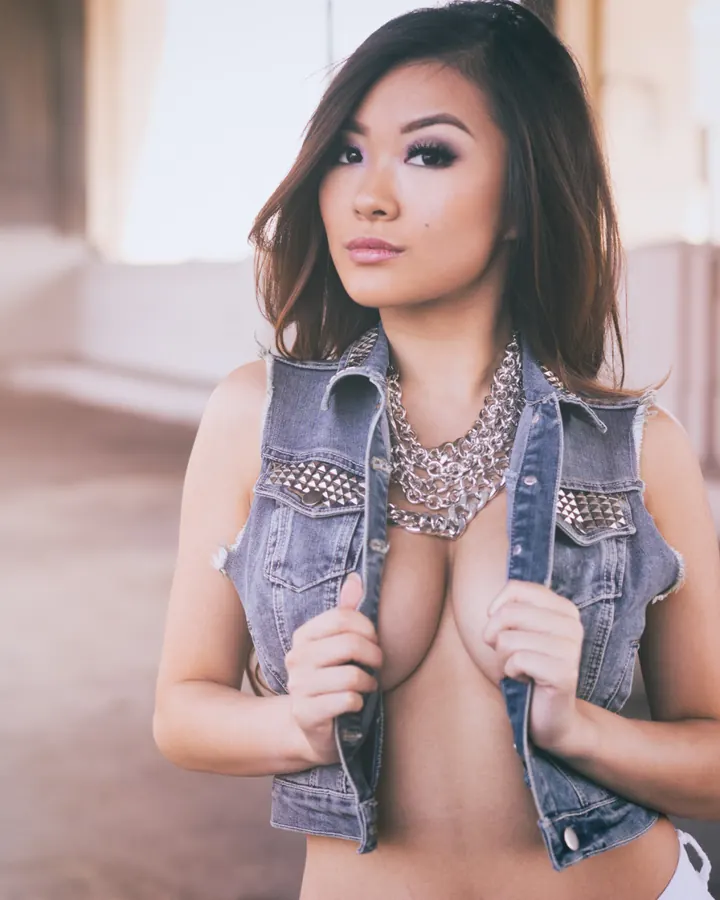 Femme asiatique en gilet en jean déchiré, tenant les bords ouverts, regard intense