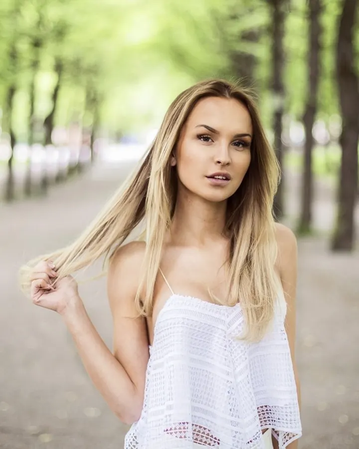 Femme aux cheveux blonds, portant un haut rouge à dentelle et un string assorti, avec des jarretières rouges, posant sur un tapis blanc dans une chambre.