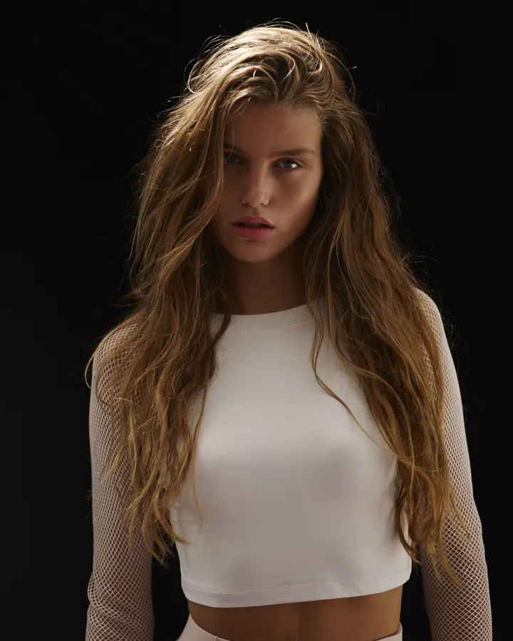 Jeune femme blonde en top blanc et jupe rose, fond noir