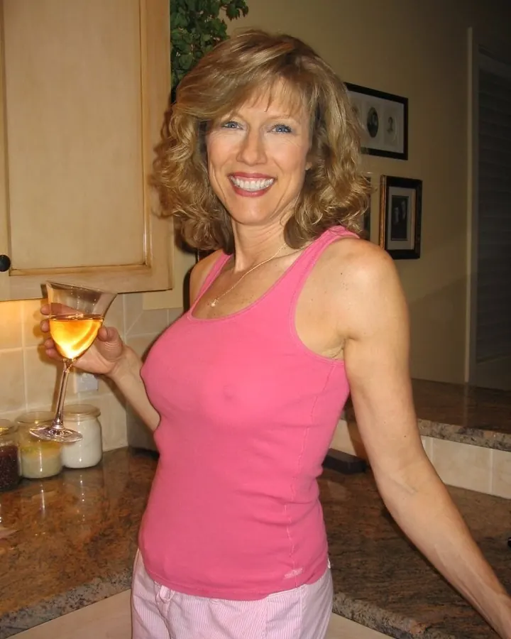 Femme blonde souriante tenant un verre de vin, débardeur rose