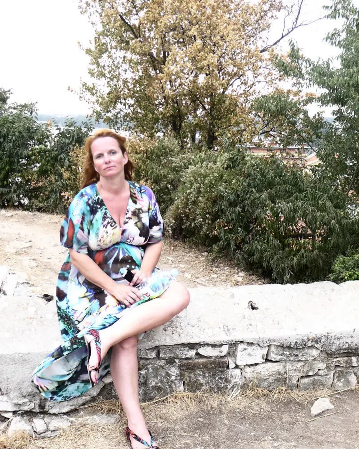 Femme rousse assise sur un muret, robe colorée