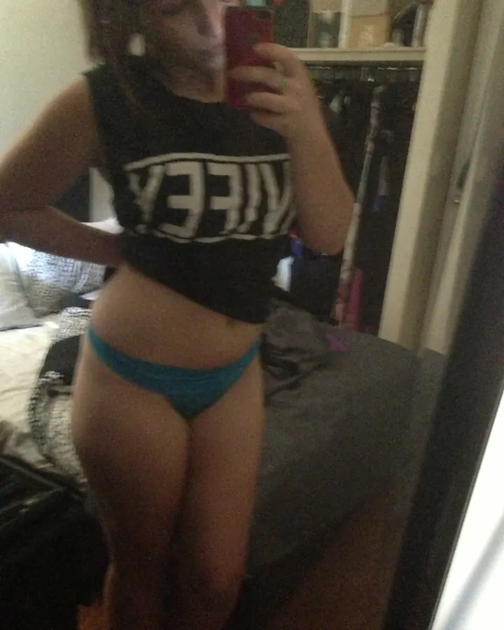 Jeune femme en haut noir et sous-vêtement bleu, prenant un selfie devant un miroir.