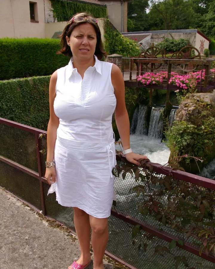 Femme en robe blanche debout près d'une rivière avec des roues à eau en arrière-plan